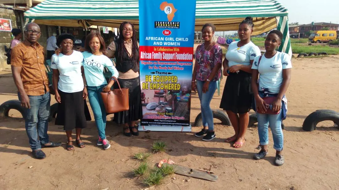 Seven foundation team members and volunteers standing in front of the 'African Girl Child and Women – Be Equipped Be Empowered' banner at an outdoor event.